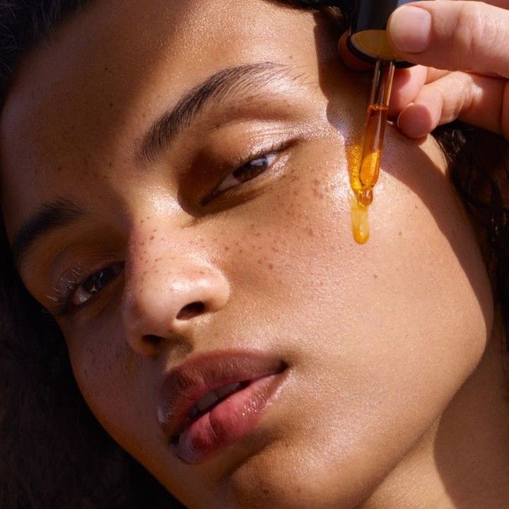 Girl with radiant, clear skin applying facial oil to her face, looking indulgent and satisfied, showcasing the nourishing effects of natural serums and oils.