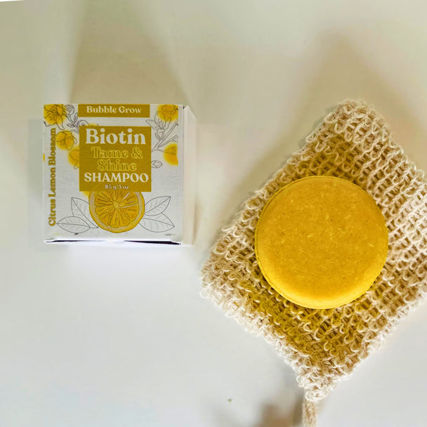 Bright yellow shampoo bar with biotin, rice protein, Argan Oil and essential oils alongside package box and sisal soap pouch against white background representing natural australian haircare.
