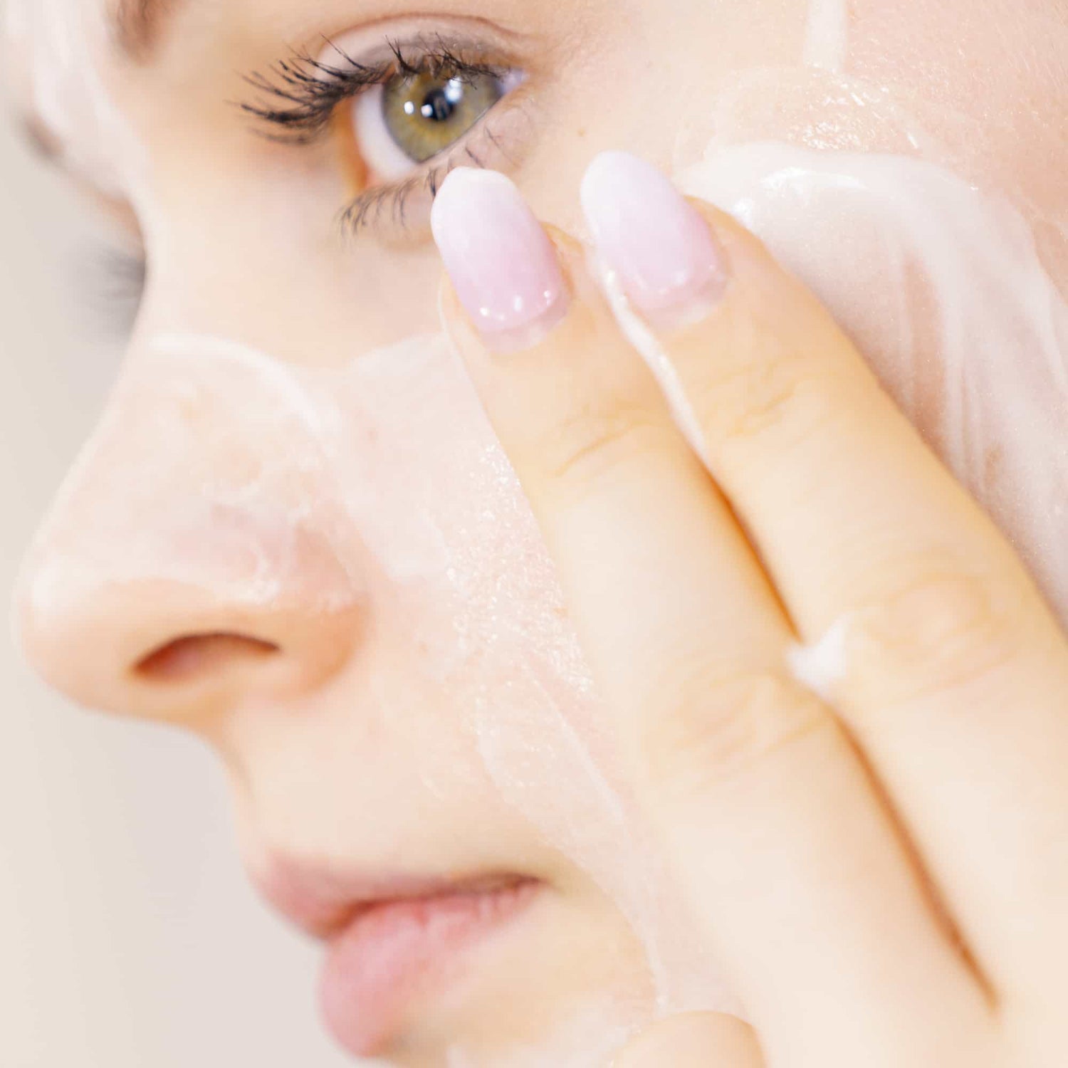 Smiling girl with a light green natural mask, surrounded by organic skincare products and fresh natural ingredients like lemon, cucumber, and peas, creating a serene, spa-like atmosphere.
