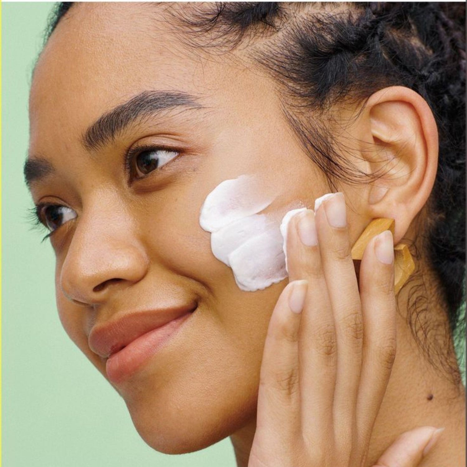 close up of a girl's smiling face applying natural moisturizer  against clean background representing natural clean skincare essentials.