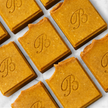 Several rectangular turmeric soap bars  arranged diagonally on a white marble surface. Each bar is embossed with a cursive letter B representing best natural brightening soap australia.