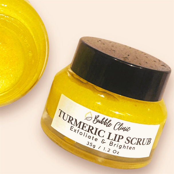 Glass clear jar with black lid of natural turmeric lip scrub revealing bright yellow hue of the lip scrub with partial image of open jar of the scrub highlighting soft creamy texture of the lip scrub. 