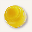 Close up of tilted open jar of the turmeric lip scrub revealing the soft creamy texture and bright yellow hue from the organic turmeric oil used in the lip scrub. 
