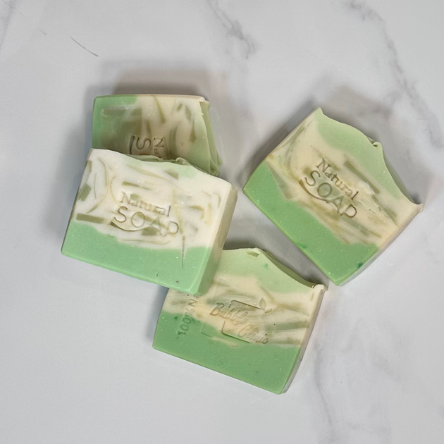 Four white and green natural brightening Kojic acid soap on a light marble background.