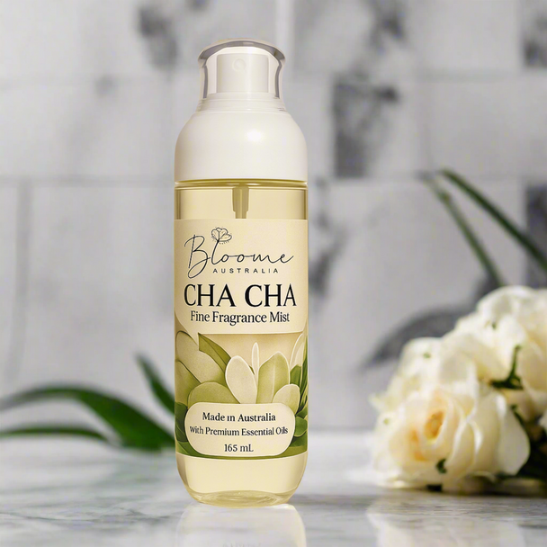 Fine fragrance body spray bottle against on a light grey marble countertop with botanicals and white flowers highlighting natural essential oils of the fragrance.