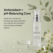 Bubble Clinic Antioxidant Toning Mist facial spray bottle displayed on a clear acrylic stand with decorative botanical elements and water droplets on a pale sage green background. Text on the left describes antioxidant and pH-balancing care ingredients.