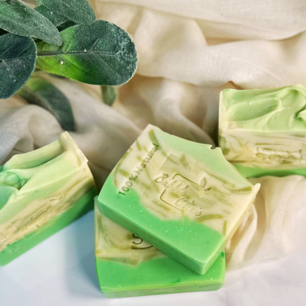 Natural brightening Kojic Acid & Alpha Arbutin Soap in green and beige, set against an organic backdrop with botanical leaves and a soft cloth.