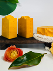 image showing natural turmeric kojic acid soap with botanicals and flowers in the foreground and background representing natural organic clean beauty and brightening skincare
