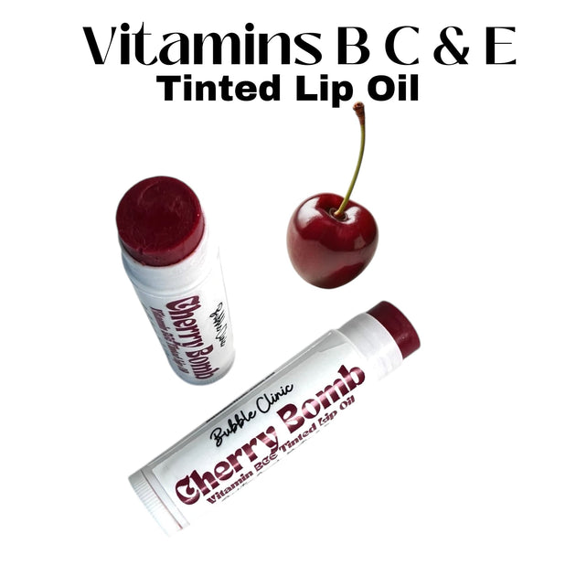 Two open tubes of Cherry Bomb Tinted Lip Oil with rich crimson tint, fresh cherry in the foreground.