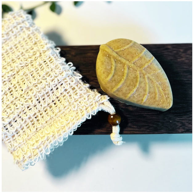 close up of leaf shaped sulphur soap bar with soap saver against white background with botanicals representing natural skincare for acne and rosacea.