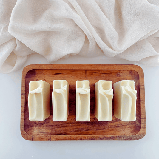 Five milky soap bars displayed on an organic wooden tray against a clean white background, showcasing their natural and gentle formulation.