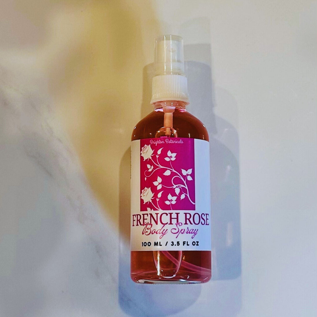 French Rose Body Fragrance Mist bottle laid flat on a light marble surface, showcasing its elegant and luxurious design.