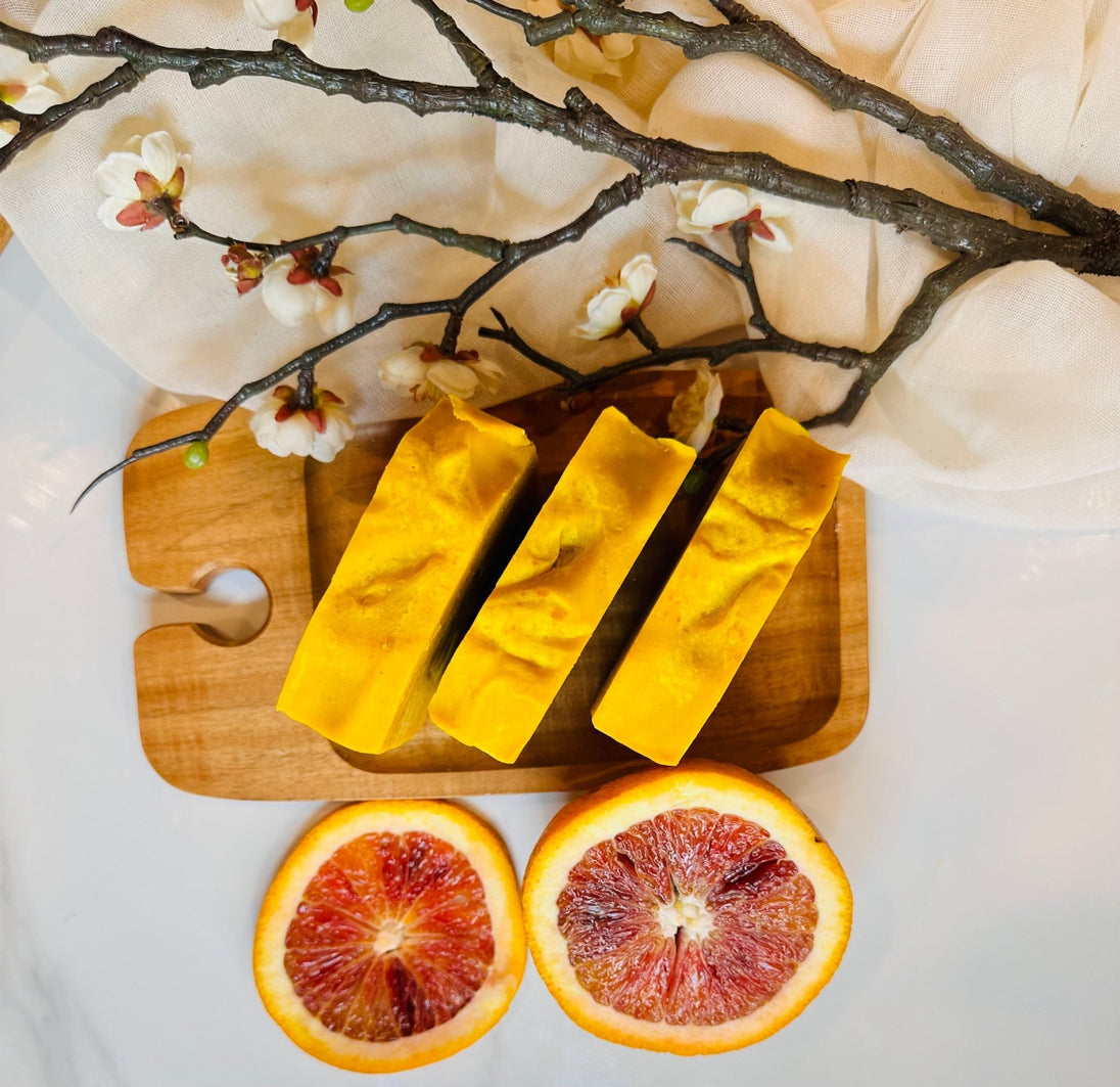Top view of bright turmeric soap bars surrounded by botanicals and citrus, highlighting organic, natural ingredients and brightening properties for radiant skin.