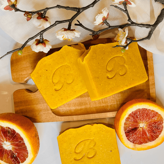 Close-up of three triple turmeric soap bars on an organic wooden tray surrounded by citrus slices and botanicals, highlighting natural ingredients and brightening properties.