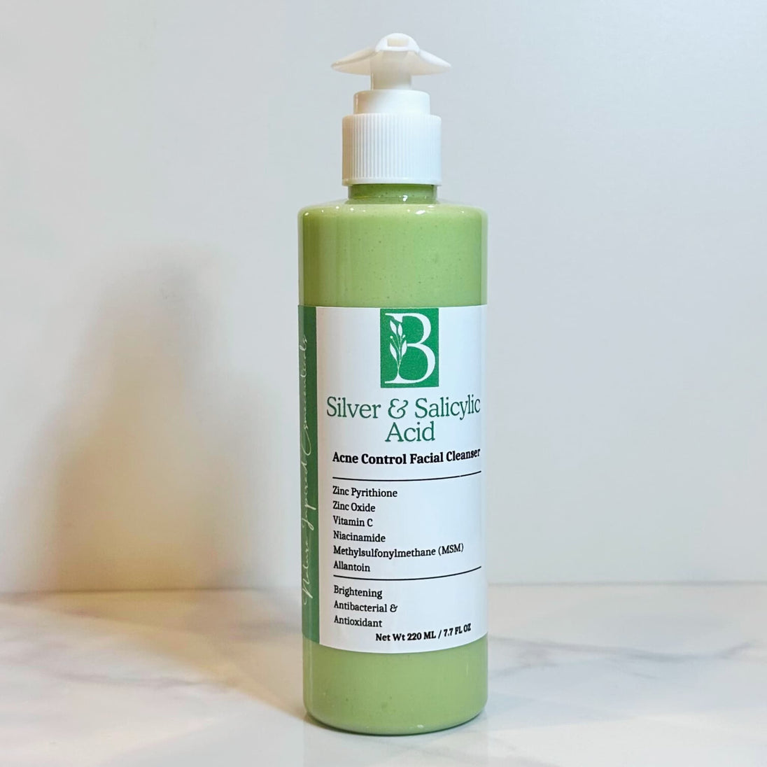 close up of acne control zinc pyrithione cleanser in clear bottle revealing creamy light green hue from comfrey and spirulina infusions on clear backdrop representing best acne treatment Australian made.