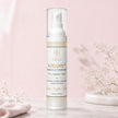 A bottle of 20% AZELUXE Azelaic Acid Radiance Treatment stands on a light marble surface against a soft pink background, styled with delicate baby's breath flowers.
