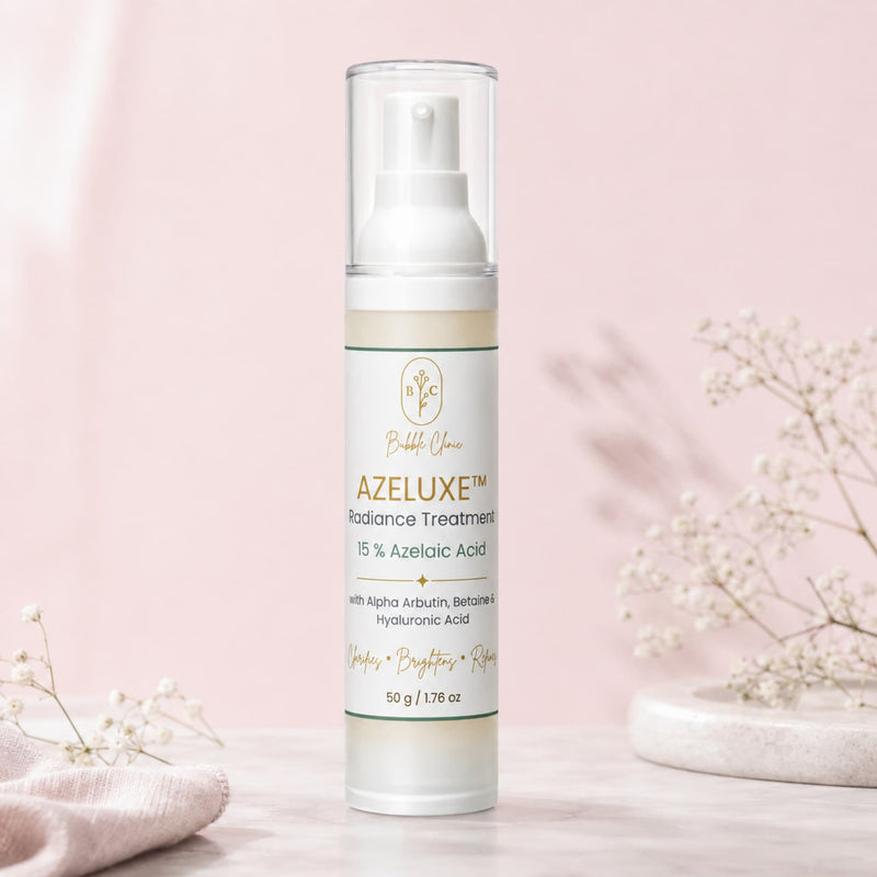 A bottle of Bubble Yours AZELUXE Radiance Treatment stands on a light marble surface against a soft pink background, styled with delicate baby's breath flowers.