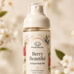 Bondi Blooms Berry Beautiful Perfume Body Mist in a clear pump bottle with a cream-colored cap and a floral label, set against a soft-focus background of white blossoms.