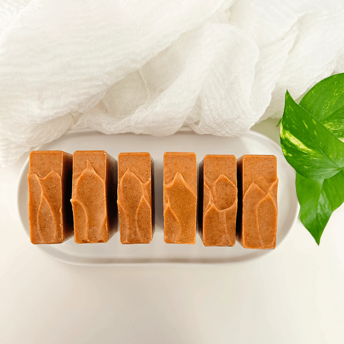 Carrot turmeric kojic acid soap bars on a white concrete tray with organic leaves and light linen, set against a white background, representing clean beauty, organic skincare, and brightening natural care.