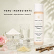 Bubble Clinic Advanced Brightening Toner bottle displayed on a clear acrylic stand with cosmetic ingredients, glass beakers, a pink rose, and dried roots highlighting botanical and science backed ingredients.