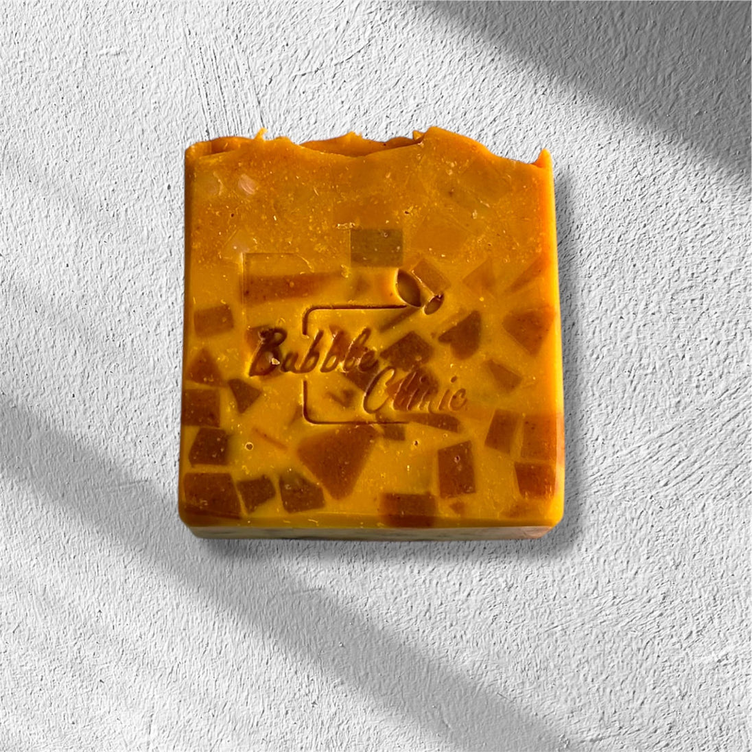 close up of carrot, turmeric kojic acid, skin lightening soap stamped with bubble clinic logo against white background.