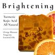 Natural Brightening Soap on white background listing primary ingredients: Turmeric, Kojic Acid, Orange Blossom & Tangerine Essential oil with fresh orange slices highlighting natural ingredients.