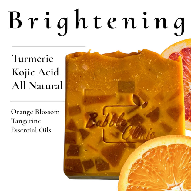 Natural Brightening Soap on white background listing primary ingredients: Turmeric, Kojic Acid, Orange Blossom & Tangerine Essential oil with fresh orange slices highlighting natural ingredients.