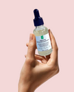 close up hand holding up glass serum bottle of brightening alpha arbutin serum with alpha arbutin against pink background representing clean beauty rituals and natural australian brightening skincare