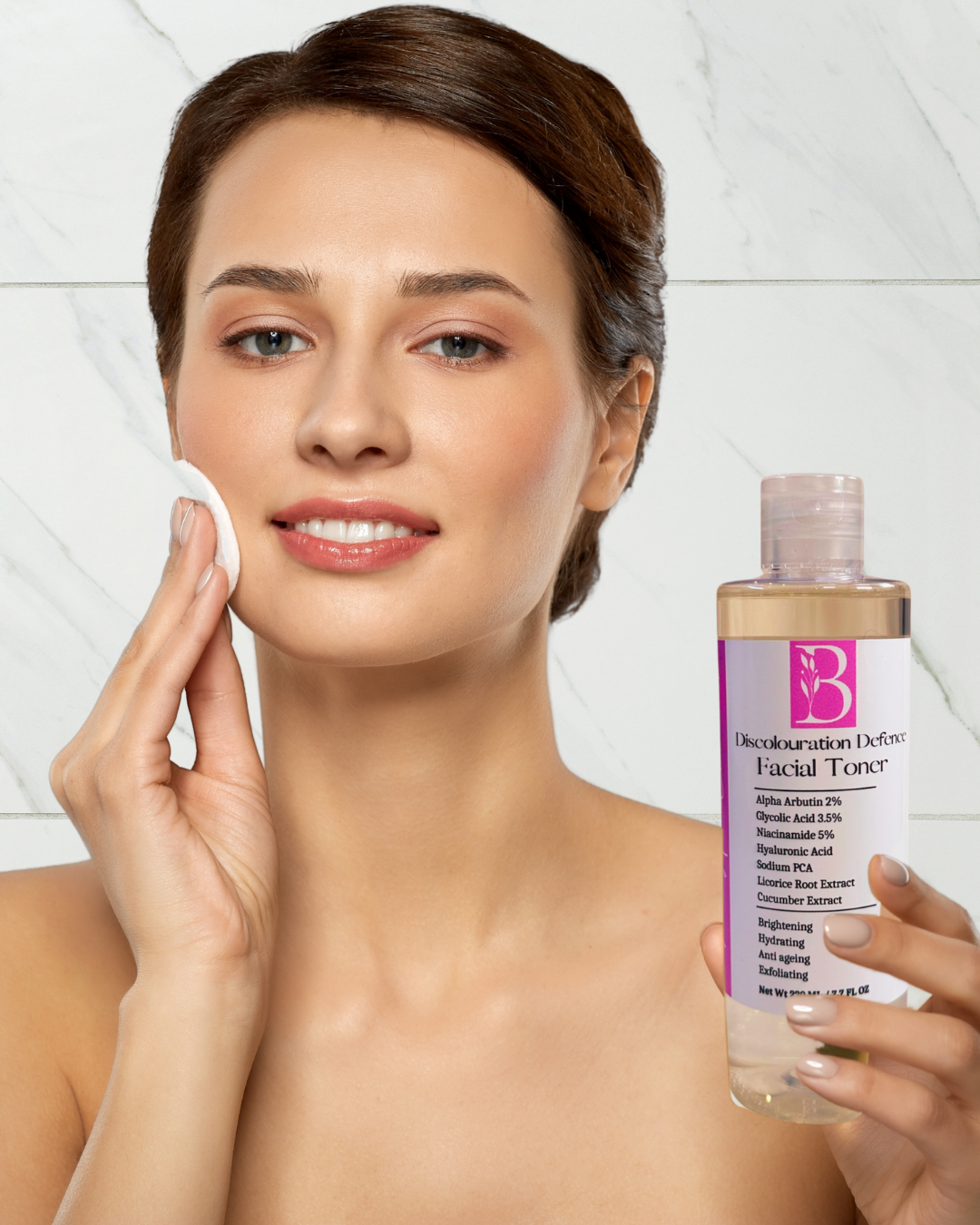 woman holding brightening kojic glycolic acid face wash bottle with alpha arbutin and using cotton round on her radiant face to apply the natural brightening toner