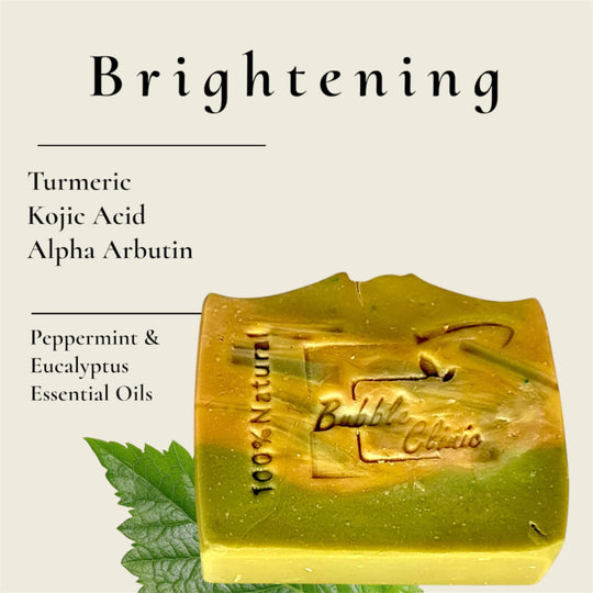 Natural brightening green and yellow soap against light background listing primary ingredients, turmeric, kojic acid, alpha arbutin and peppermint and eucalyptus essential oils.