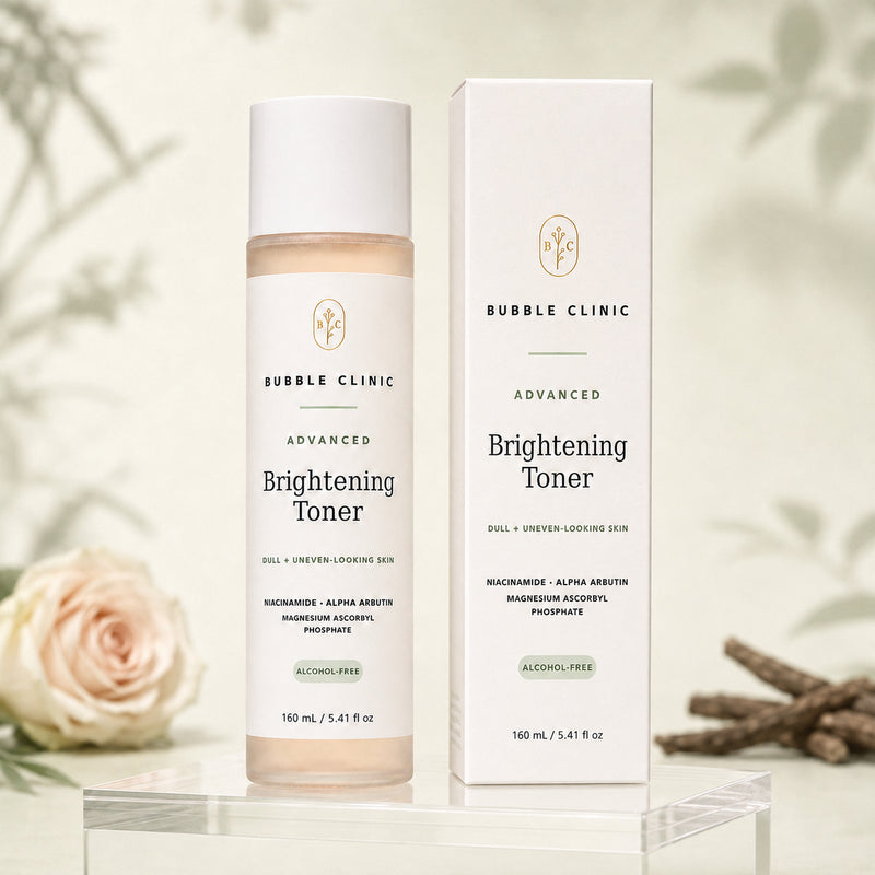 Bubble Clinic Advanced Brightening Toner bottle and matching outer box displayed on a clear acrylic stand, with a soft beige background and decorative rose and branch props.