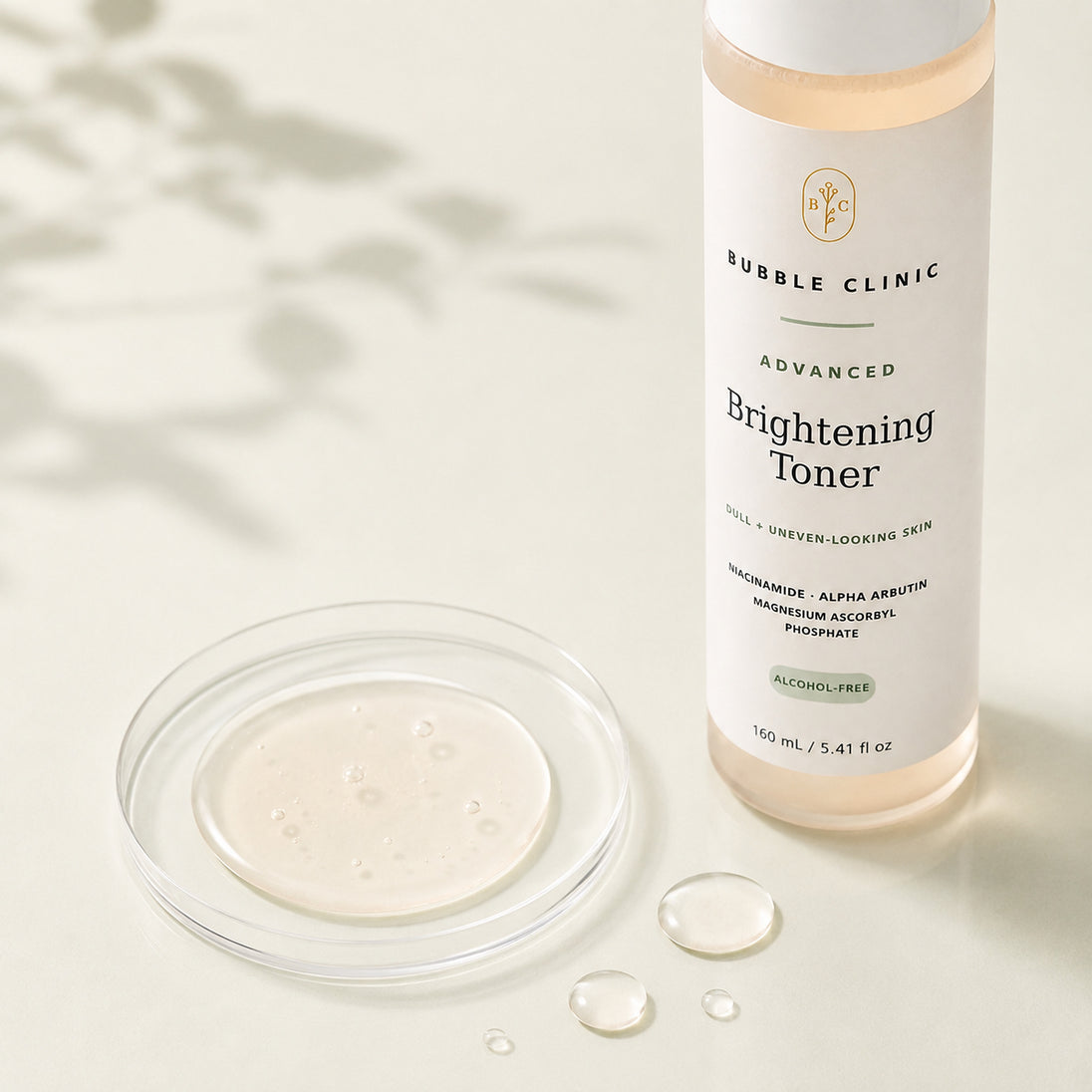 Bubble Clinic Brightening Toner bottle with a clear glass dish of pale cream serum and a few liquid droplets on a light beige surface with soft leaf shadows.