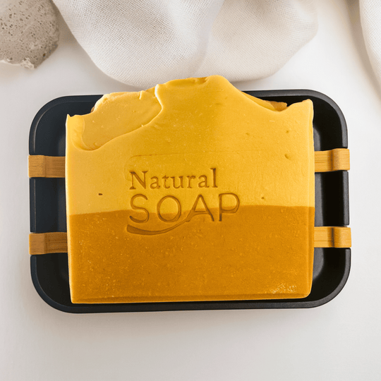 two tone brightening kojic acid soap with chamomile essential oil and turmeric on black soap dish against white background representing natural skincare.