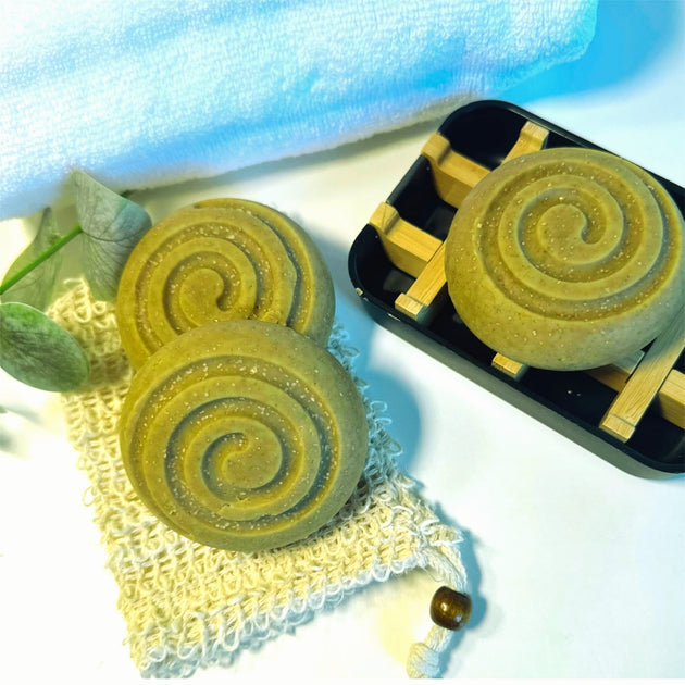 close up of circular sulphur bars infused with comfrey, wheatgrass and spirulina for acne and rosacea with towel and botanicals in the background representing organic acne skincare solutions.