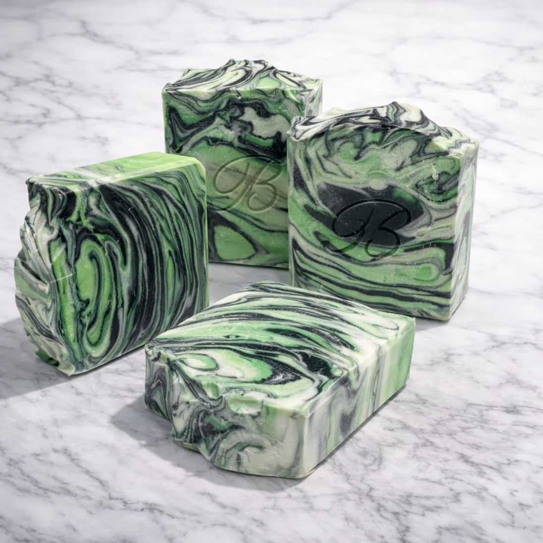 Green and black marbled kojic peppermint soap bars with activated charcoal on a marble surface representing best natural brightening soaps Australian made.