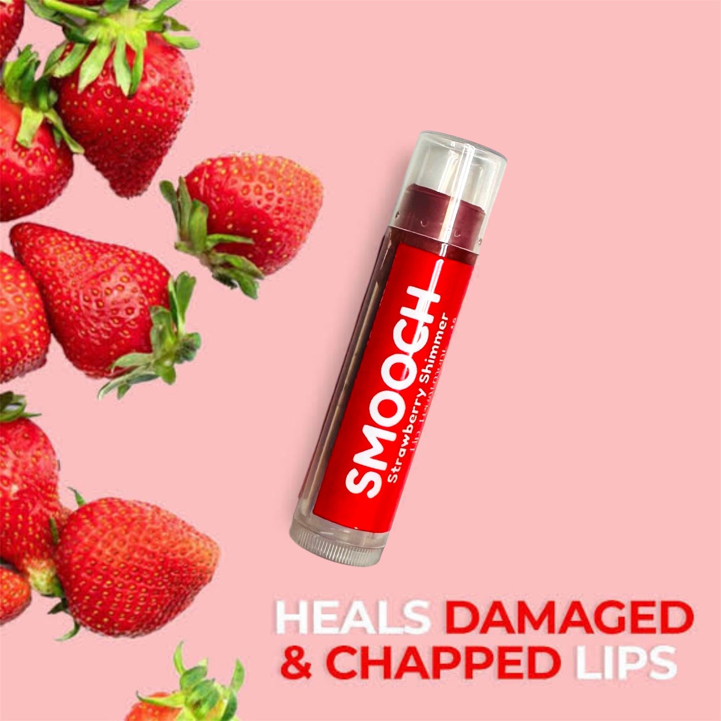 Strawberry lip balm against a pink background with fresh strawberries and text reading "Heals damaged and chapped lips," highlighting its nourishing and hydrating benefits.

