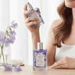 Female holding a bottle of luxury 'Sweet Pea' hair perfume with flowers in a vase and bright sunny background representing natural Australian Haircare.
