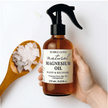 Bottle of natural magnesium oil with a label, held by a hand, next to a wooden spoon with magnesium flakes representing pure Australian Magnesium Oil