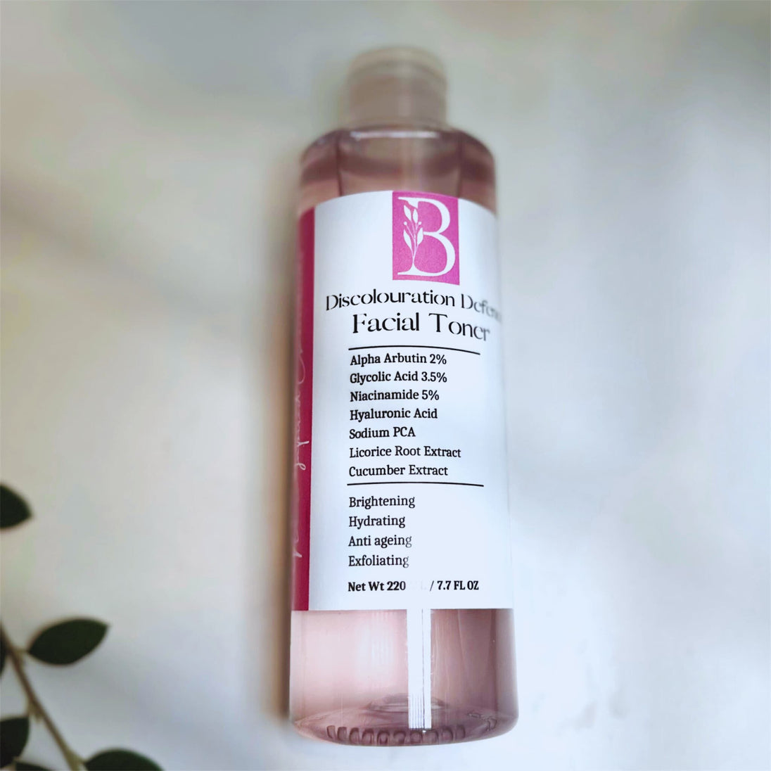 bottle with brightening dark spots defence toner with alpha arbutin and glycolic acid on white background with botanicals representing natural Australian brightening skincare.