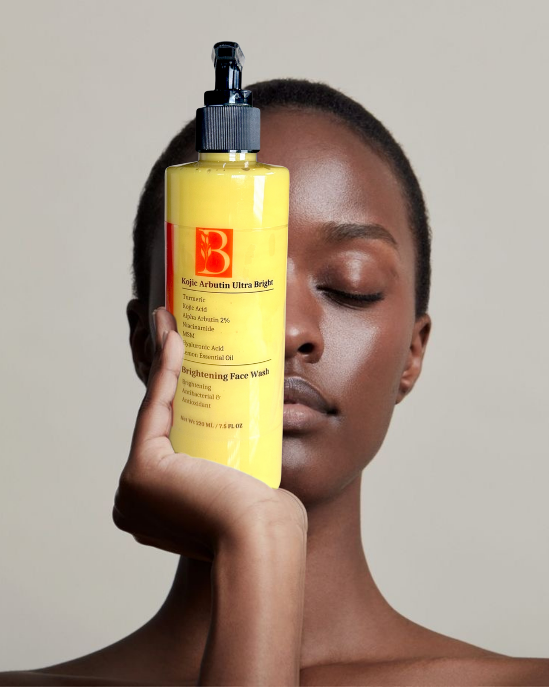 woman with short hair and dark radiant beautiful skin tone holding up to her face bottle of turmeric kojic acid face wash with alpha arbutin representing brightening skincare for all ski types