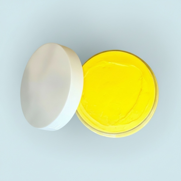 Open container of yellow natural turmeric cream on a light green background