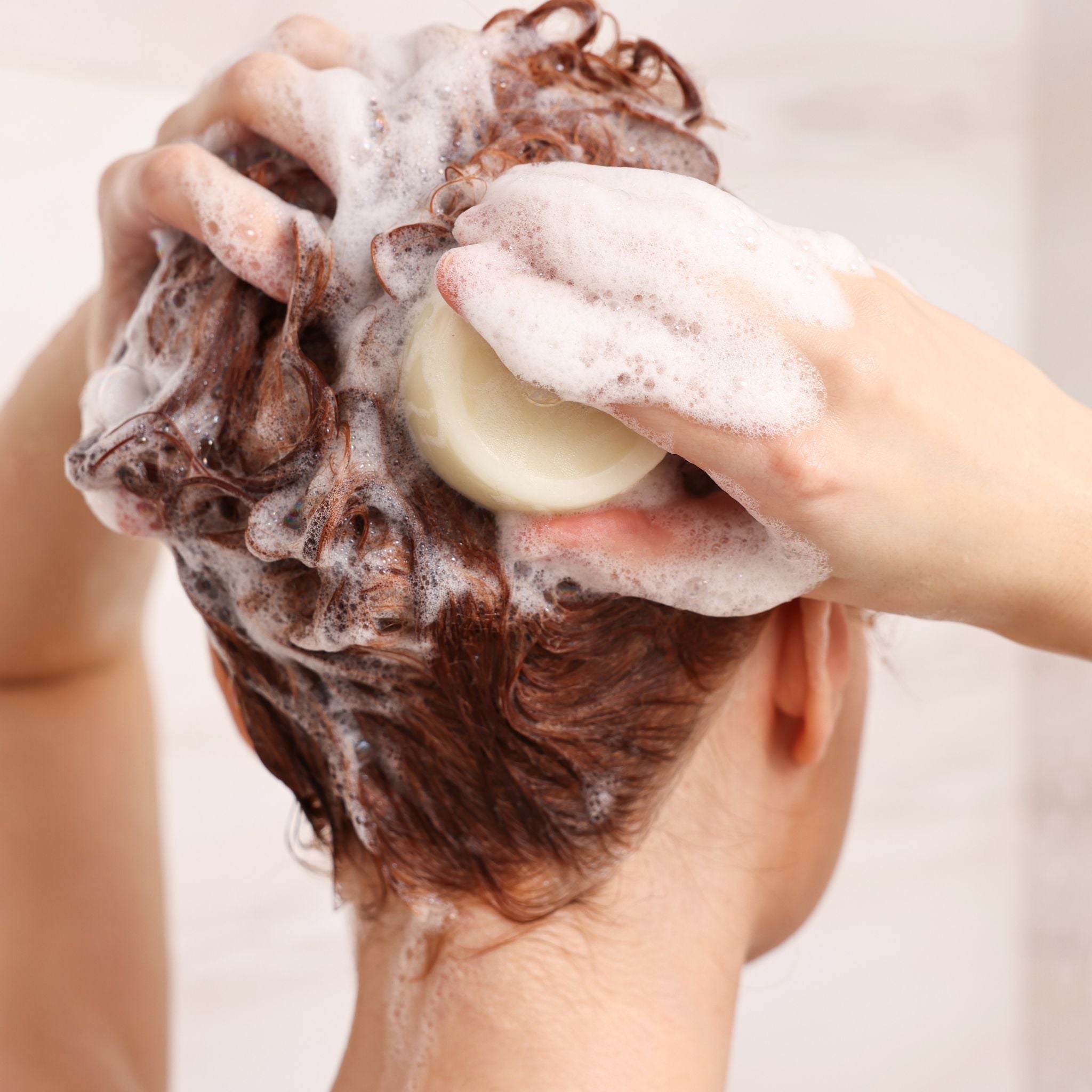 Close up of woman's head under the shower using natural shampoo bar with creamy lather representing natural australian haircare.