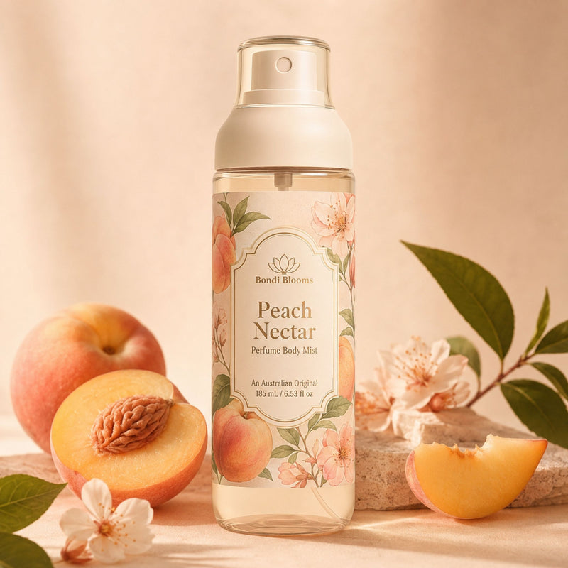 A bottle of Peach Nectar Perfume Body Mist stands centered on a warm beige surface, surrounded by fresh peaches, peach halves, leaves, and blossoms. The bottle has a cream pump and a floral label with peach illustrations.