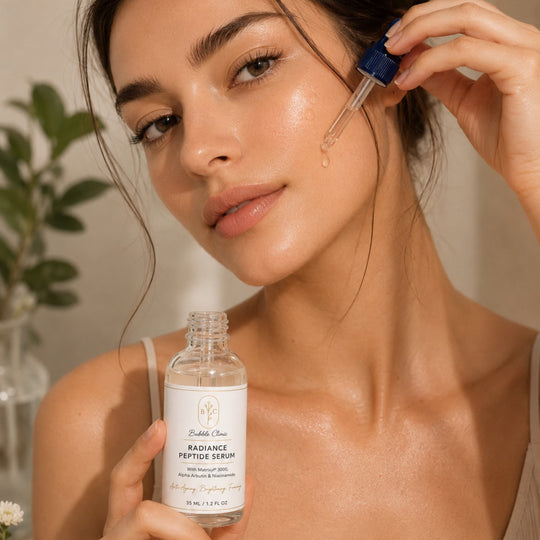 Radiance Peptide Serum with matrixyl 3000 and alpha arubutin being applied by a woman to her cheeck in a warm neutral background and soft-focus greenery representing best brightening peptide serum Australia.