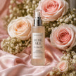Bottle of 'Rose Silk' hair product surrounded by pink roses on a pink fabric background