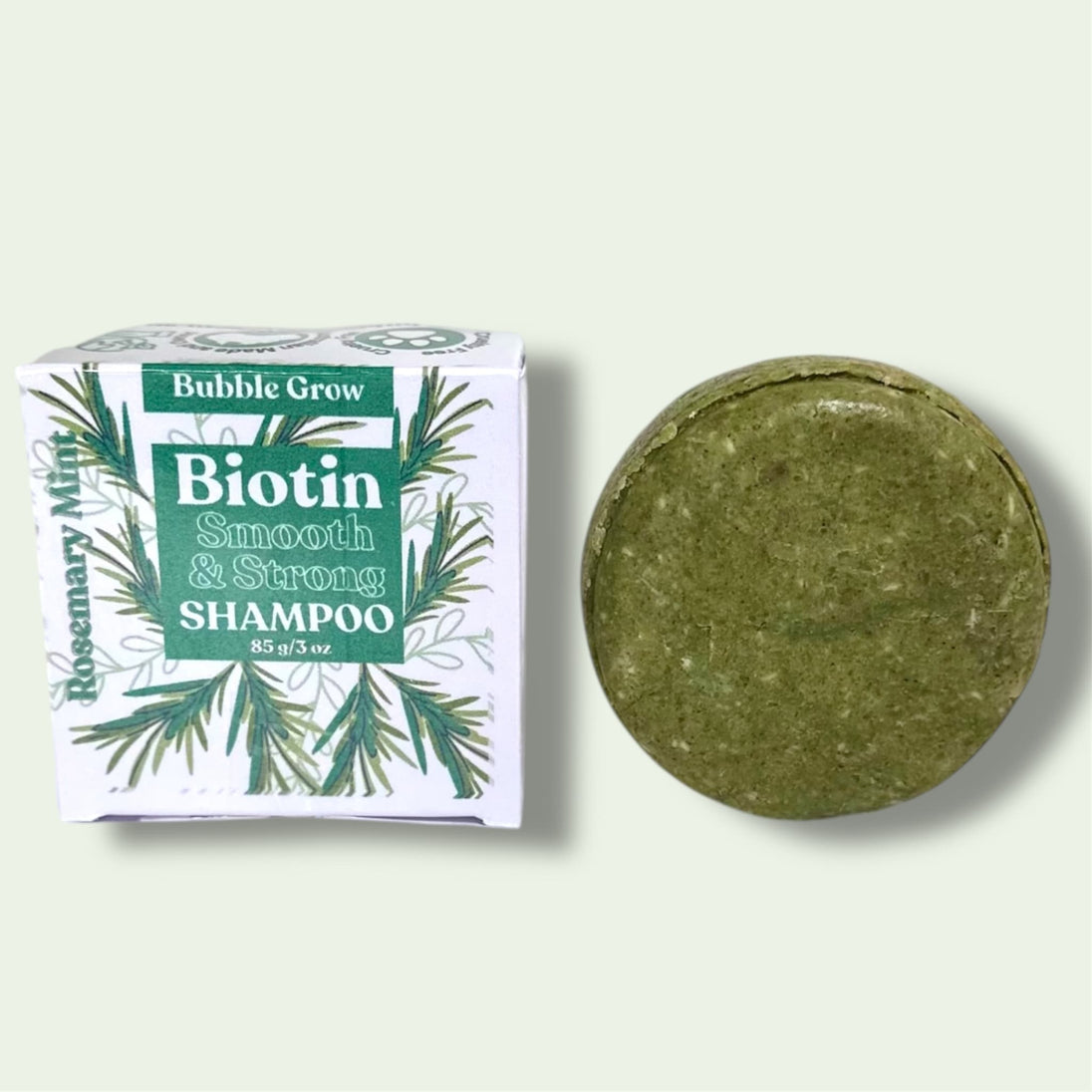 Biotin & Rosemary Shampoo Bar. Infused with spirulina, amla oil, and refreshing peppermint for scalp health and shine on a lime background with package box. Sulfate-free and natural.