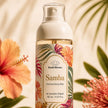Bondi Blooms Samba Perfume Body Mist in a 185 mL pump bottle, featuring a tropical floral label with hibiscus and palm leaves, set against a warm beige background with blurred tropical flowers and leaves.