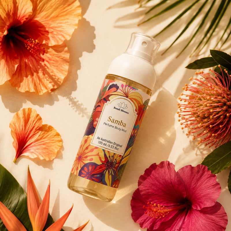 A bottle of Samba Perfume Body Mist by styled in a flat-lay with tropical hibiscus flowers and palm leaves on a warm beige background.