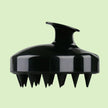 close up of soft silicone scalp brush - black with splash of water against white background. soft bristles stimulate hair growth and remove dandruff, awaken hair follicles.