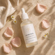 Silver Rose Skin Rescue Serum flat lay with rose petals and chamomile on a warm beige background.